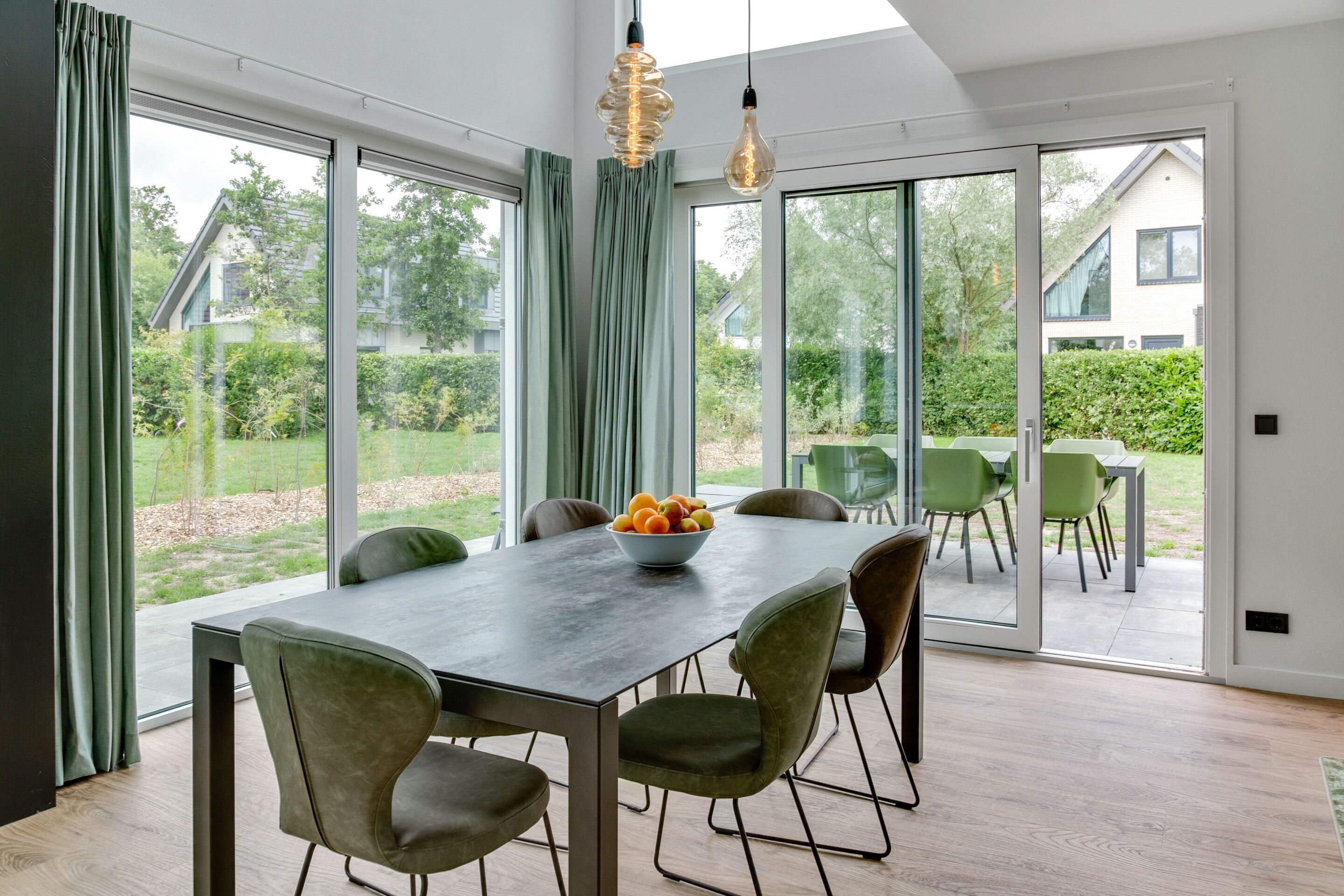 A modern dining area with a large table, six chairs, and a bowl of fruit.