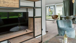 Un soggiorno moderno con una grande televisione a schermo piatto, scaffali in legno, una poltrona blu e un'area pranzo con tavolo e sedie.