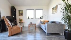 Ein modernes Wohnzimmer mit Ledersessel, grauem Sofa, Couchtisch und einem großen Fenster mit zwei Scheiben.