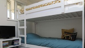 A bunk bed room with a television on a white stand, a bookshelf with DVDs, and a woven rug on the floor.