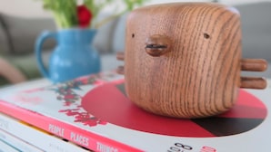 A wooden mug with a face on a table with books and a blue vase with flowers.