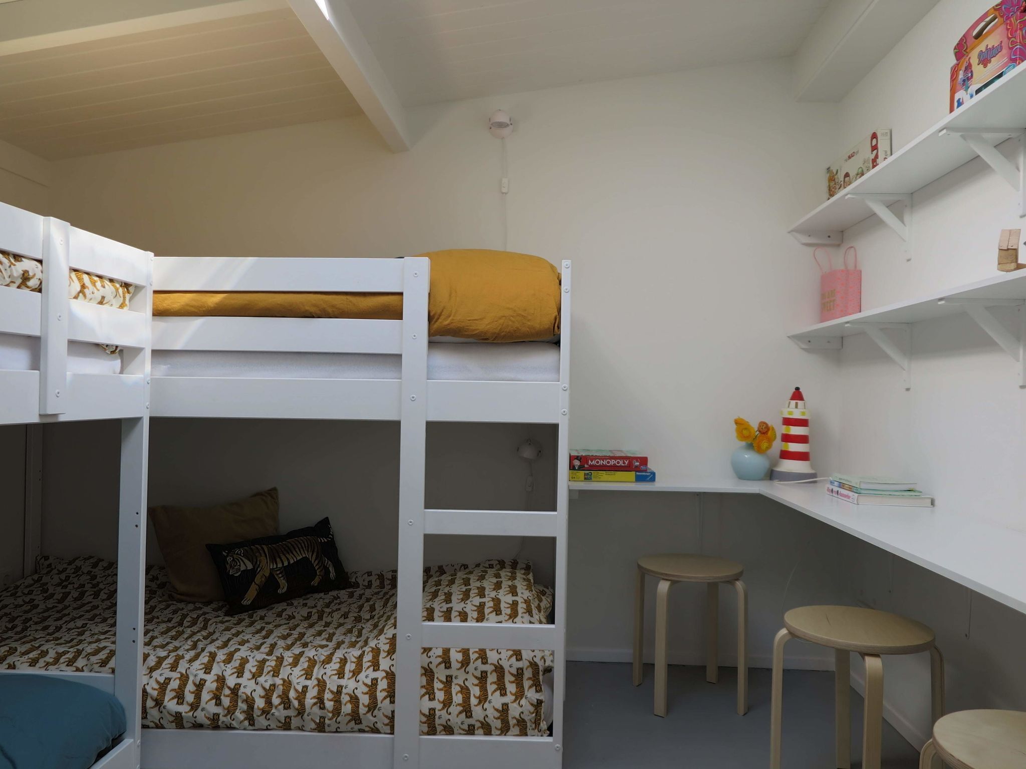 A bunk bed room with a desk and two stools.