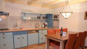 Une cuisine avec un coin repas, comprenant une table en bois, des chaises orange et un luminaire suspendu.