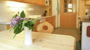 A kitchen with wooden cabinets, a white vase with flowers on a wooden table, and a door with a window.
