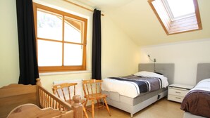 A bedroom with a bed, a desk, a chair, a dresser, and a window with curtains.