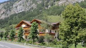 A hotel with multiple wooden balconies, surrounded by lush greenery and a mountainous backdrop.