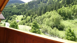 A wooden balcony overlooking a lush valley with dense forests and a distant mountain. - Bright Holiday Home in Huttschlag near Mountains Ski Slopes (Huettschlag)