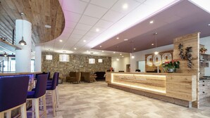A reception area with a wooden reception desk, stone wall, and seating area with purple chairs. - Apartment in Gosau With a Shared Sauna (Gosau)