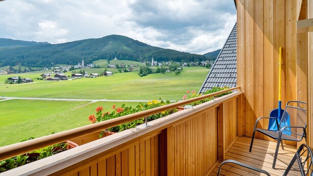A wooden balcony with a view of a green landscape and distant buildings. - Apartment in Gosau With a Shared Sauna (Gosau)