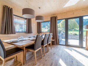 Un comedor con una mesa y sillas de madera, ventanas amplias y cortinas.
