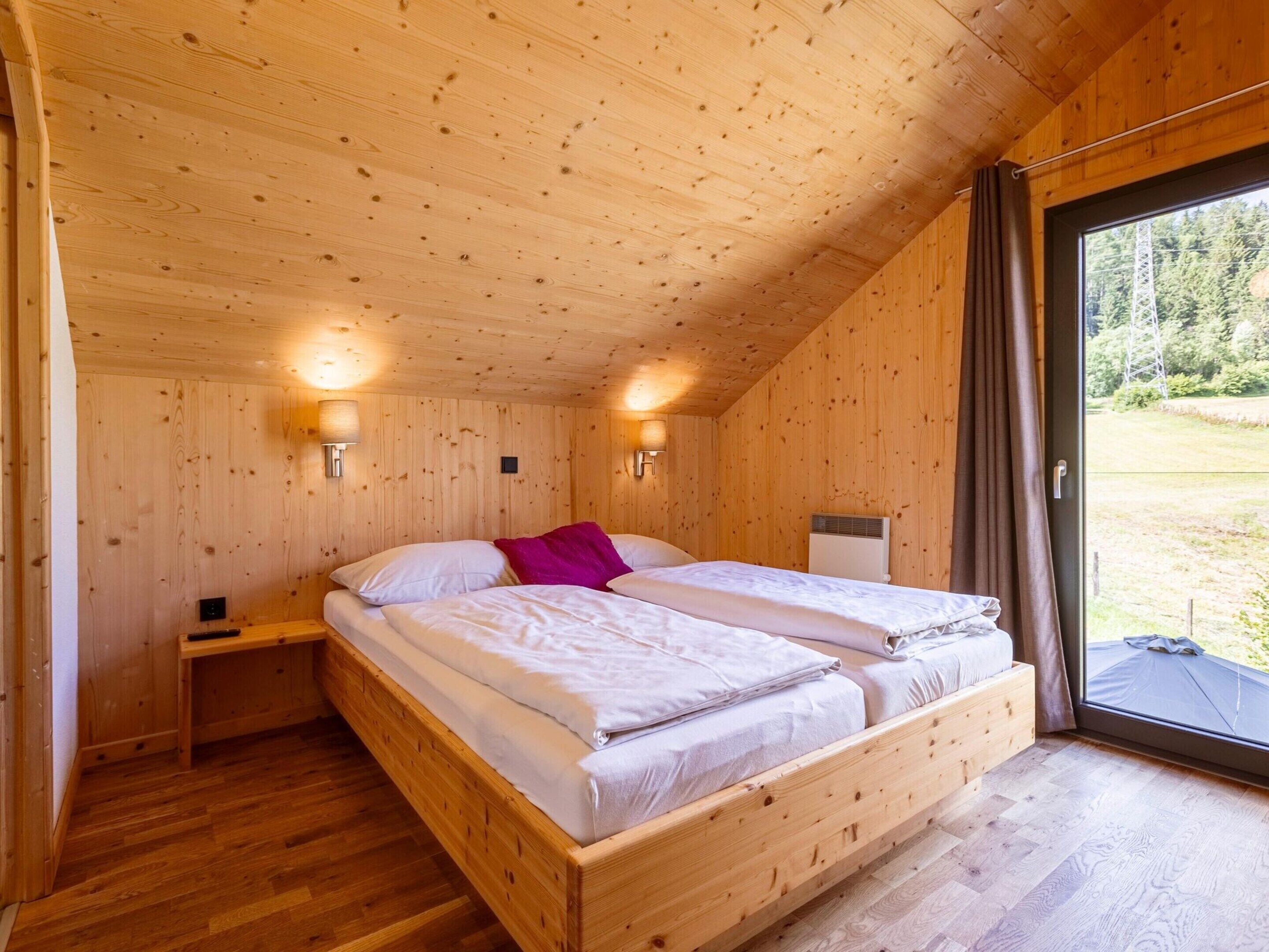 A wooden cabin bedroom with two beds, a nightstand, and a window with curtains.