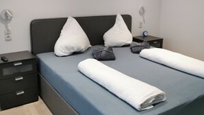 A neatly made bed with a blue mattress, two white pillows, and a folded white towel. There is a small bedside table with a clock and a remote control. - Apartment in Oetz Near Ski Lift (Oetz)