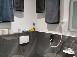 Egy fürdőszoba törölközőtartóval, WC-papírral, hajszárítóval és tükörrel.