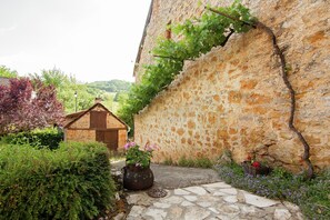 A stone wall with a vine, a small wooden structure, and a stone pathway. - Lakeside Cottage Roziers Retreat (Chasteaux)