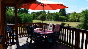 A wooden deck with a table and chairs, an umbrella, and a view of a forested area. - Chalet du Lac - Nature Escape (Beaulieu)