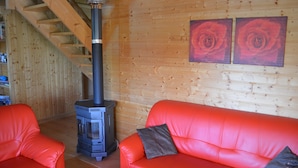 A wooden interior with a red leather sofa, a wood-burning stove, and a staircase. - Chalet du Lac - Nature Escape (Beaulieu)