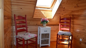 A room with wooden walls, a skylight, two red chairs with floral cushions, and a white side table with baskets. - Chalet du Lac - Nature Escape (Beaulieu)