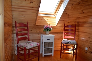 A room with wooden walls, a skylight, two red chairs with floral cushions, and a white side table with baskets. - Chalet du Lac - Nature Escape (Beaulieu)