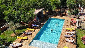A rectangular swimming pool with a wooden deck, surrounded by lounge chairs and umbrellas, and shaded by trees. - Villa in Poggio-mezzana Near the Sea (Poggio-Mezzana)