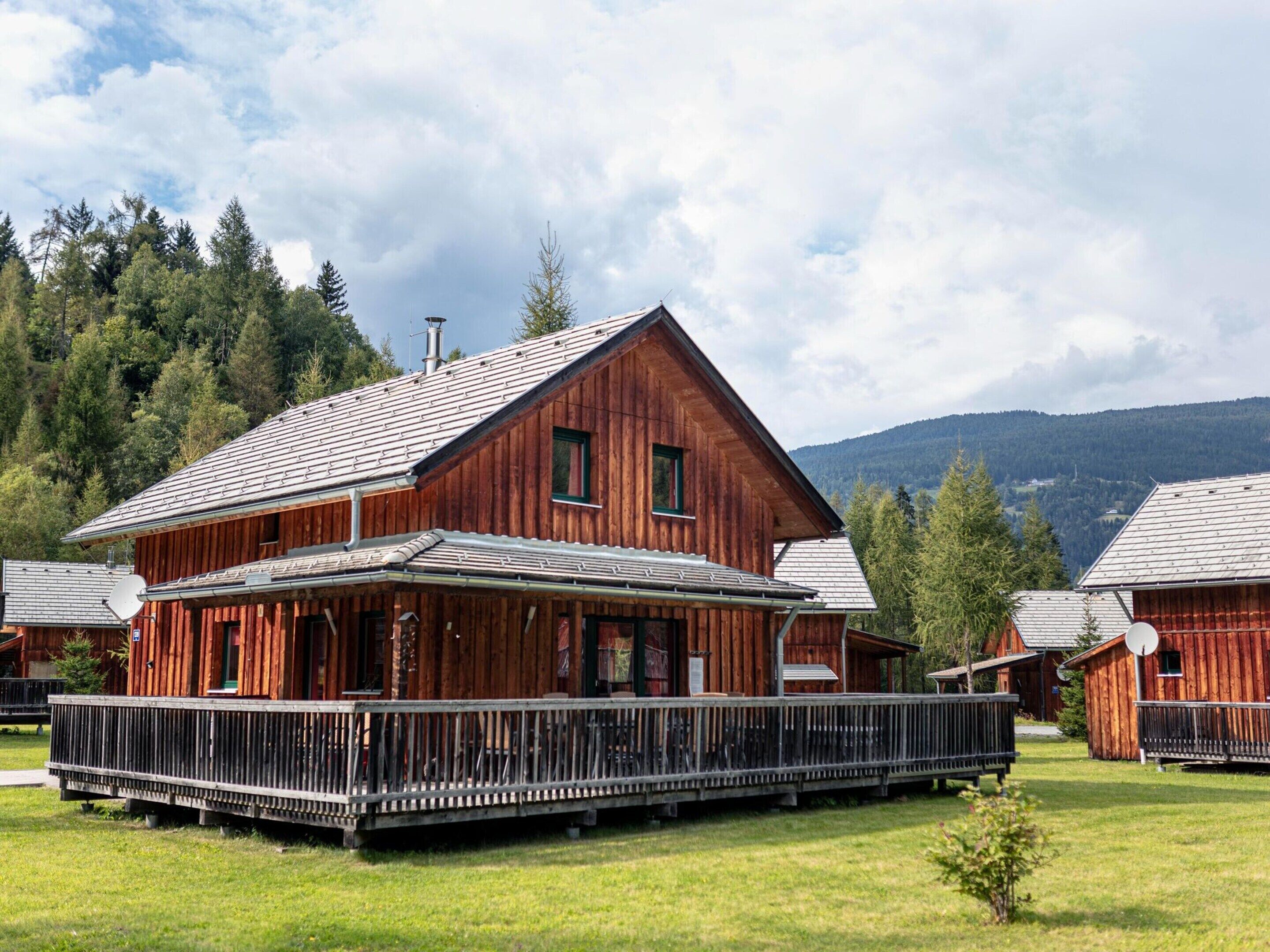 A wooden cabin with a porch and a metal roof, surrounded by a grassy area and trees.