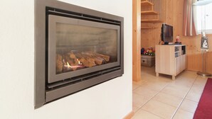 Une cheminée moderne avec une façade en verre, des poutres en bois, un téléviseur et un tapis rouge.
