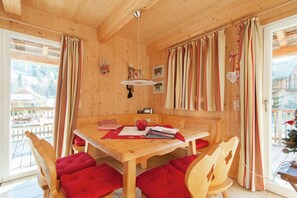 A wooden interior with a dining table, red cushioned chairs, and a view of a snowy landscape through a large window.