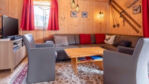 L’intérieur chaleureux d’un chalet, avec un revêtement mural en bois, un ensemble de canapés, un téléviseur et une table à manger.