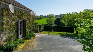 Ein Steinhäuschen mit Satellitenschüssel, Schaukel und einem Kiesweg, der zu einem grünen Feld führt.