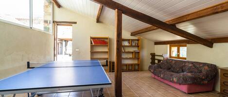 Une pièce avec une table de ping-pong, des étagères en bois, un canapé et un sol carrelé.