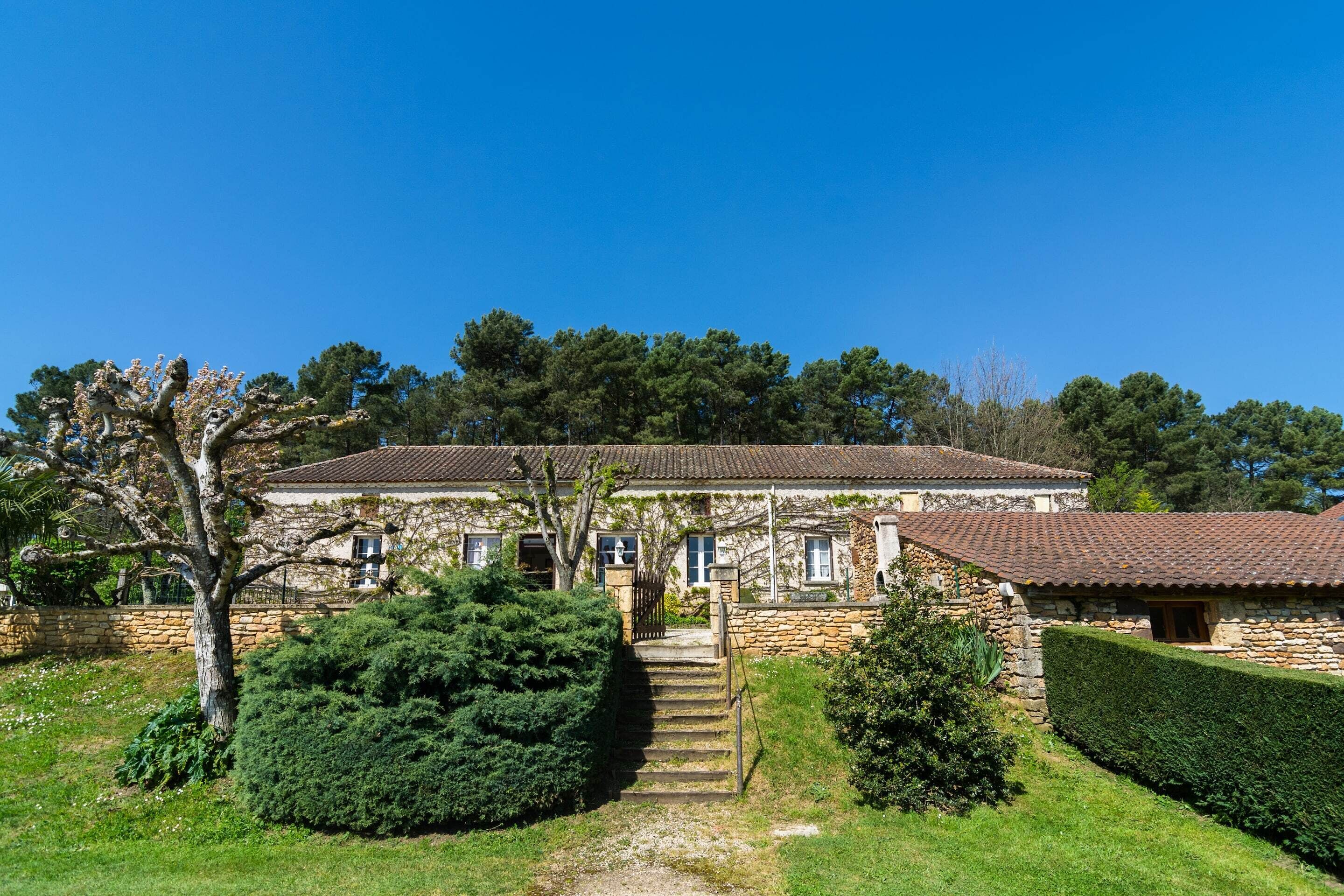 A stone house with a tiled roof, a staircase leading to the entrance, and a well-maintained garden.