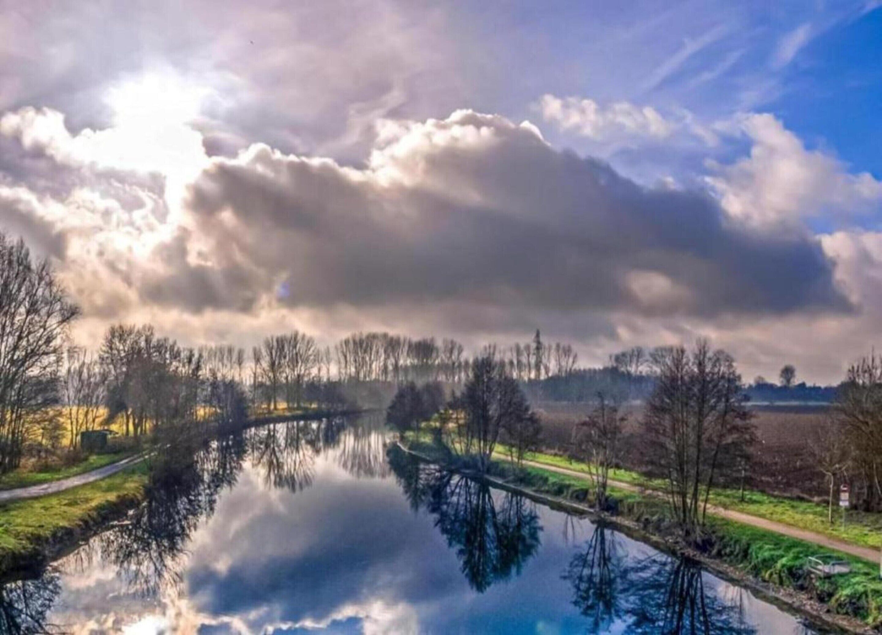 A calm river reflecting trees and a cloudy sky.