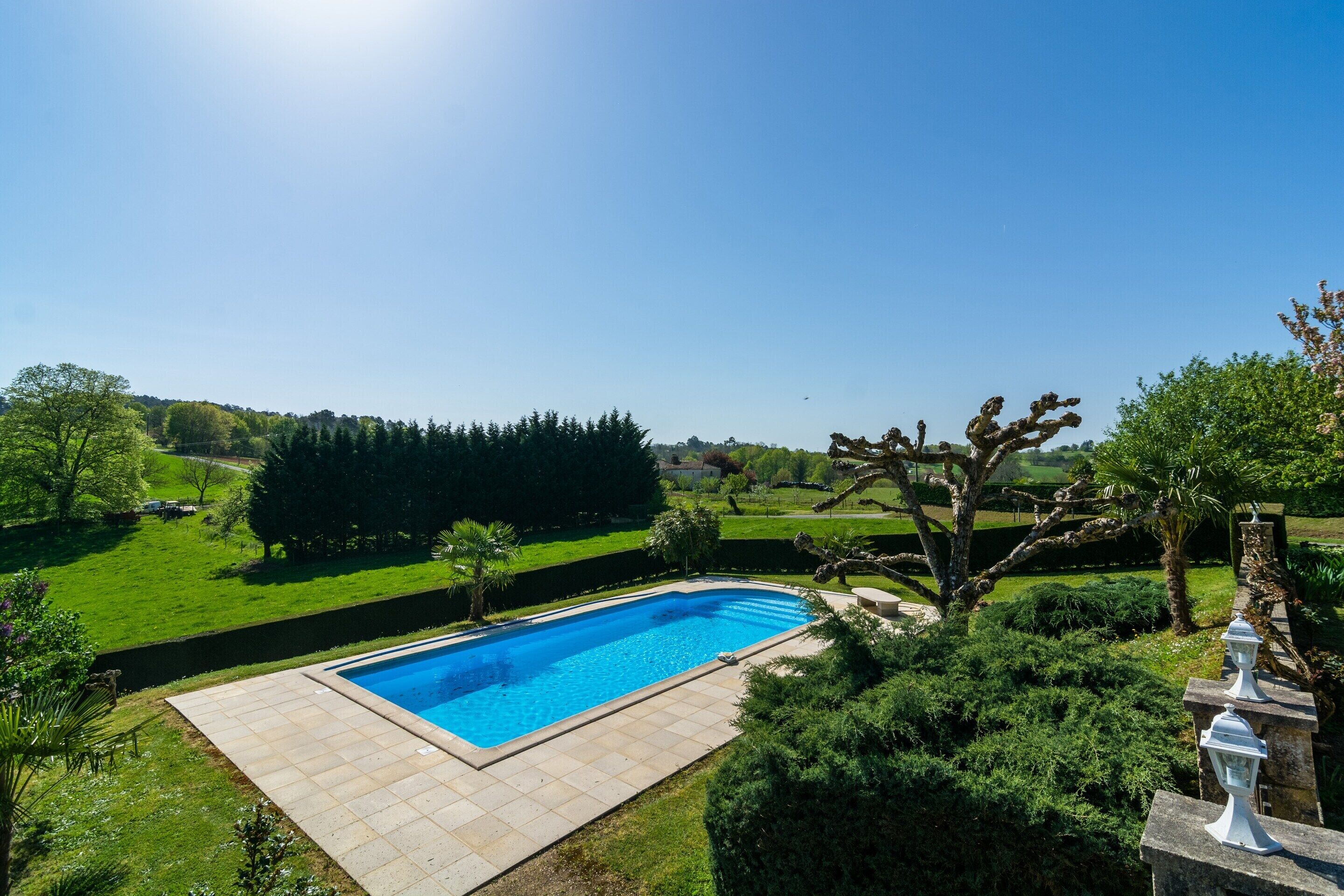 A swimming pool with a tiled deck, surrounded by well-maintained lawns and trees.