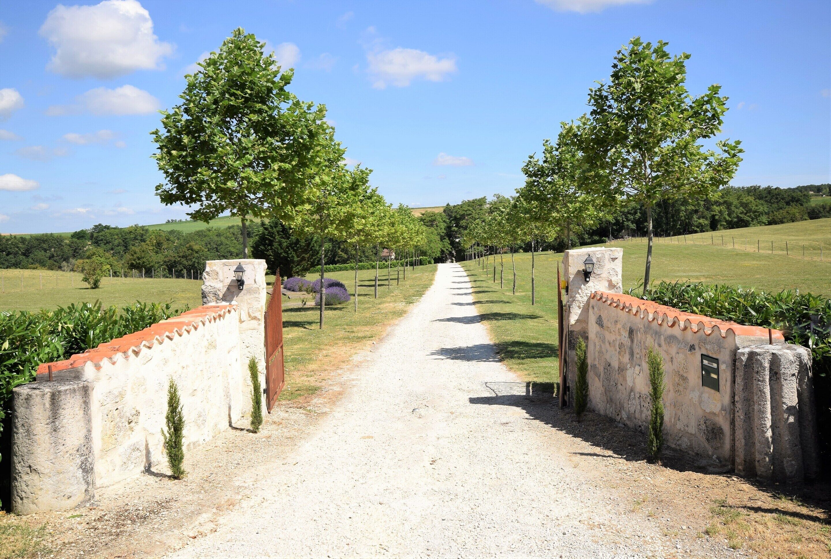 A gravel path leading through a rustic gate, surrounded by greenery and trees.