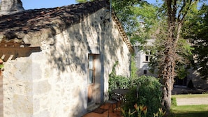 A rustic stone building with a tiled roof, a wooden door, and a small patio area with a table and chairs.