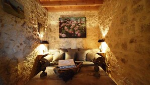 A rustic room with a wooden ceiling, stone walls, a sofa, two lamps, and a painting of flowers.