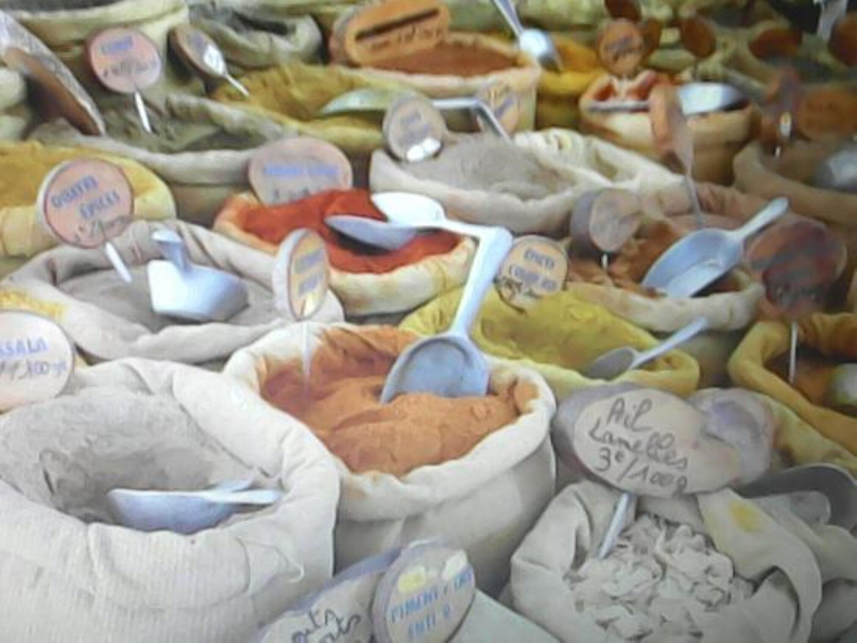 A variety of spices displayed in open containers with labels, some with measuring spoons.