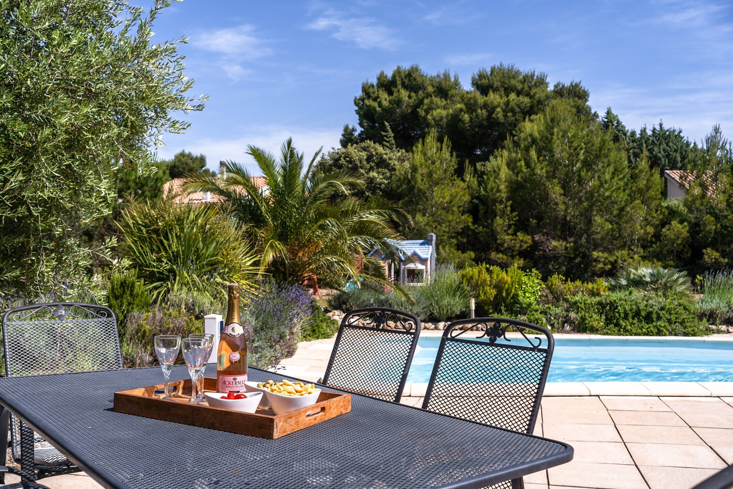 A poolside dining area with a table, chairs, and a bottle of wine.
