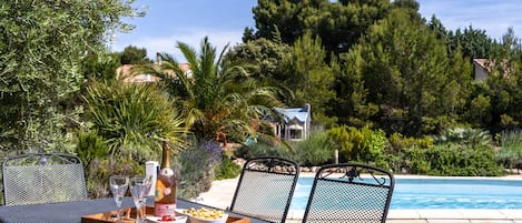 A poolside dining area with a table, chairs, and a bottle of wine.