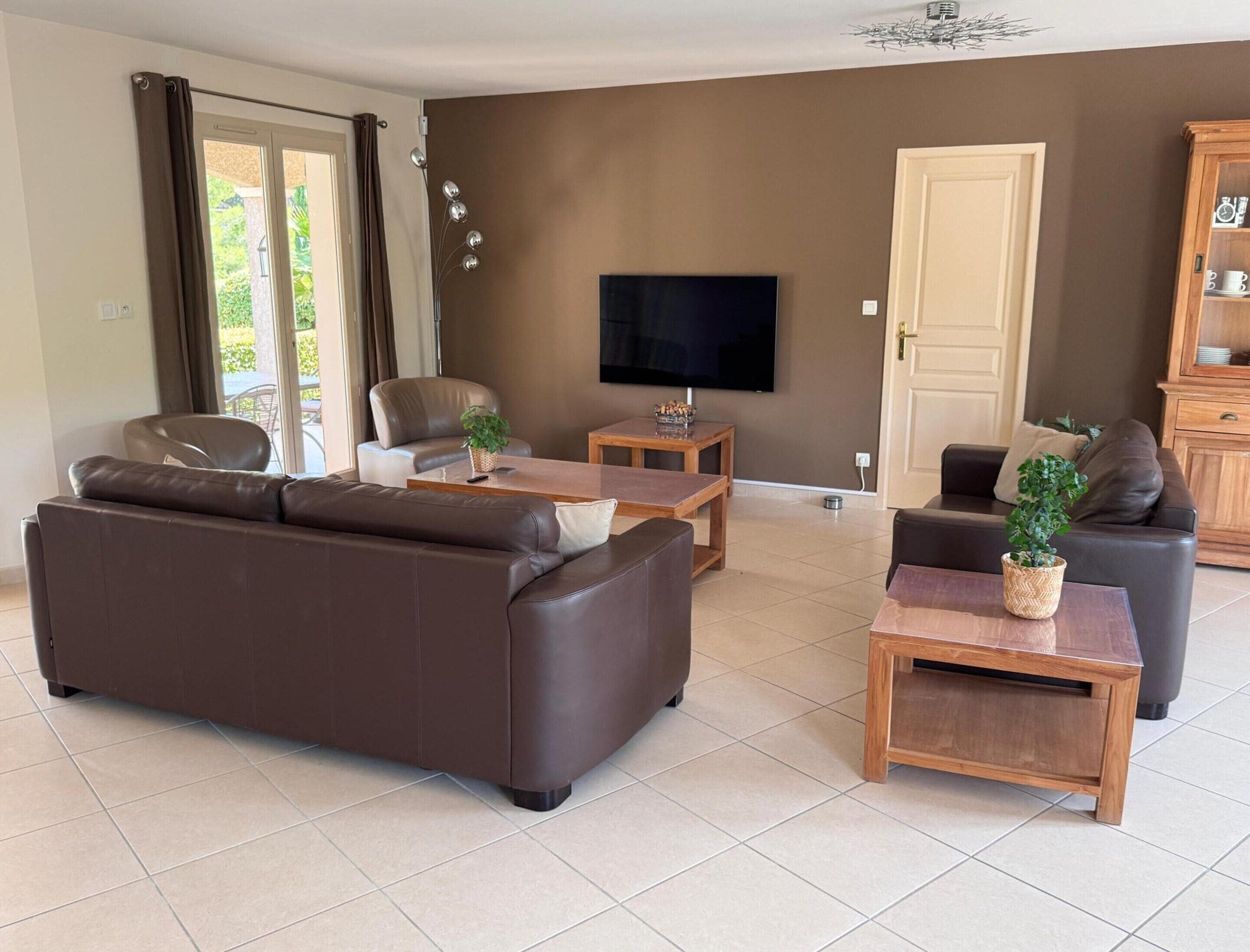 Un salon comprenant un canapé, des fauteuils, une table basse, un téléviseur et un meuble.