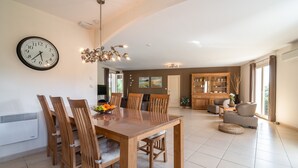 Un espacio habitable amplio con una mesa de comedor, sillas, una araña y una cocina al fondo.