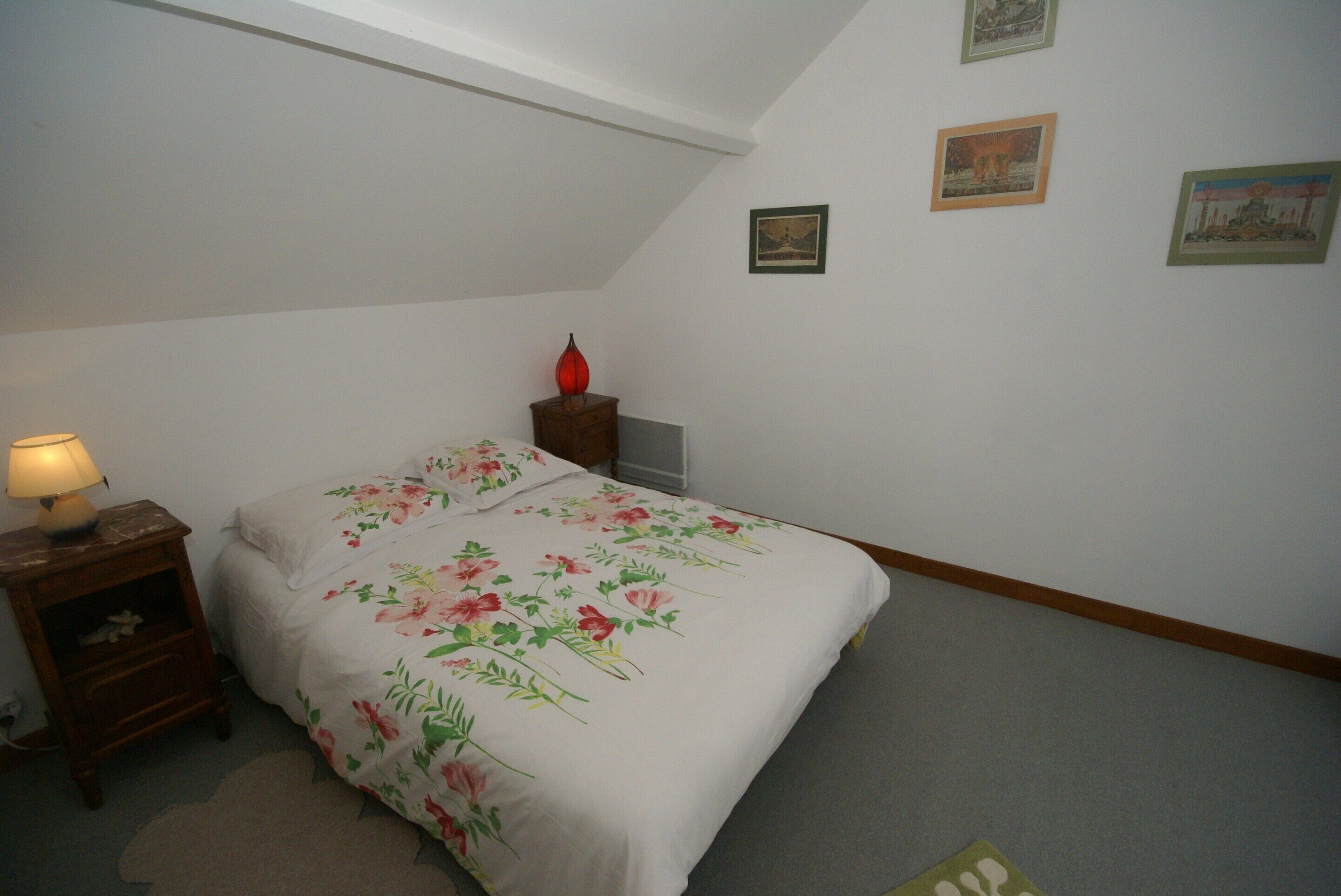 Un dormitorio con una cama, una mesita de noche, una lámpara y una pared decorada con cuadros.