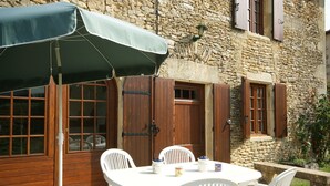 A stone building with wooden shutters, a table with chairs, and a green umbrella. - Historic Dordogne Escape (Loubejac)