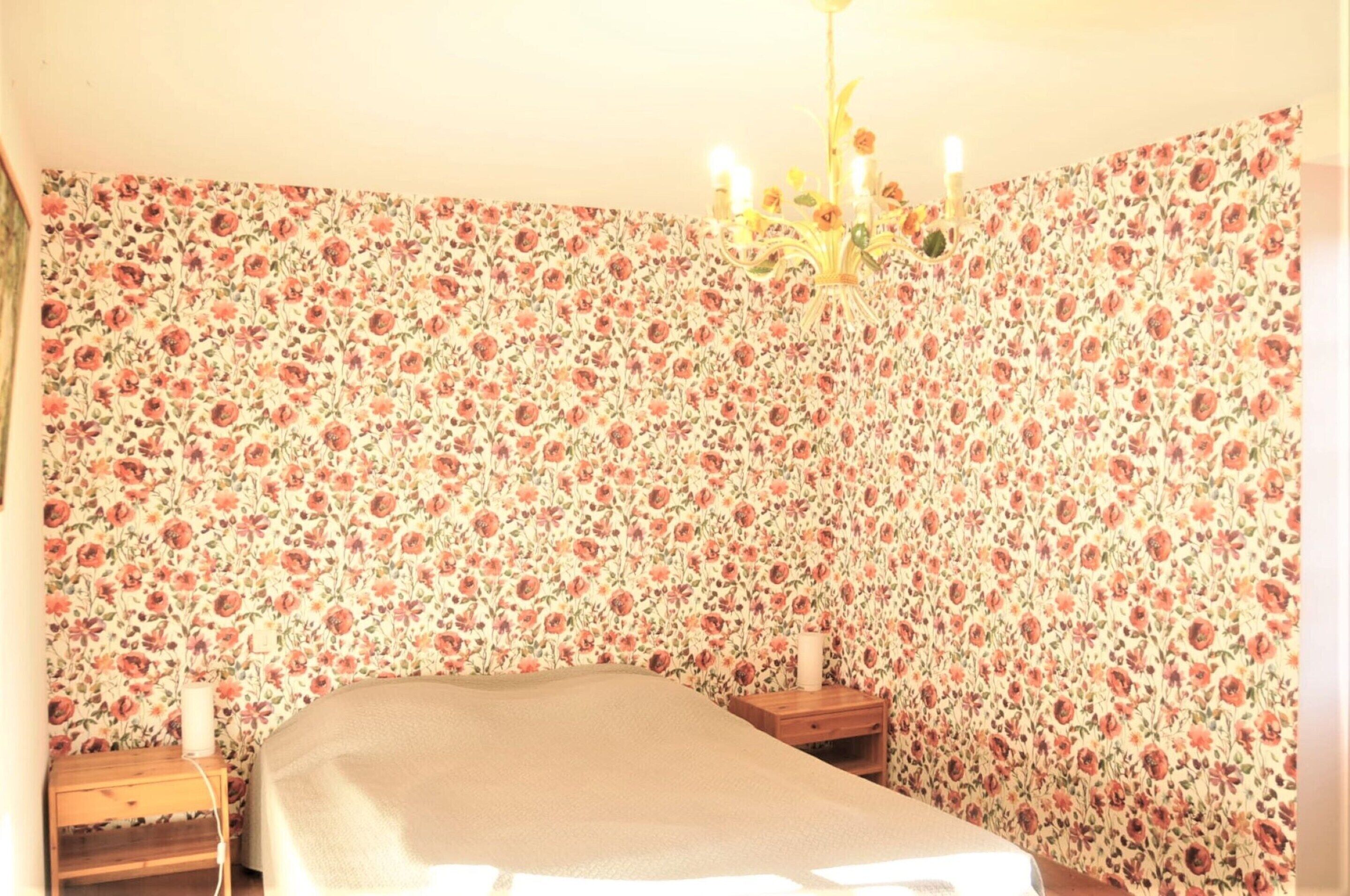 Een kamer met bloemenbehang, een bed, een nachtkastje en een kroonluchter.