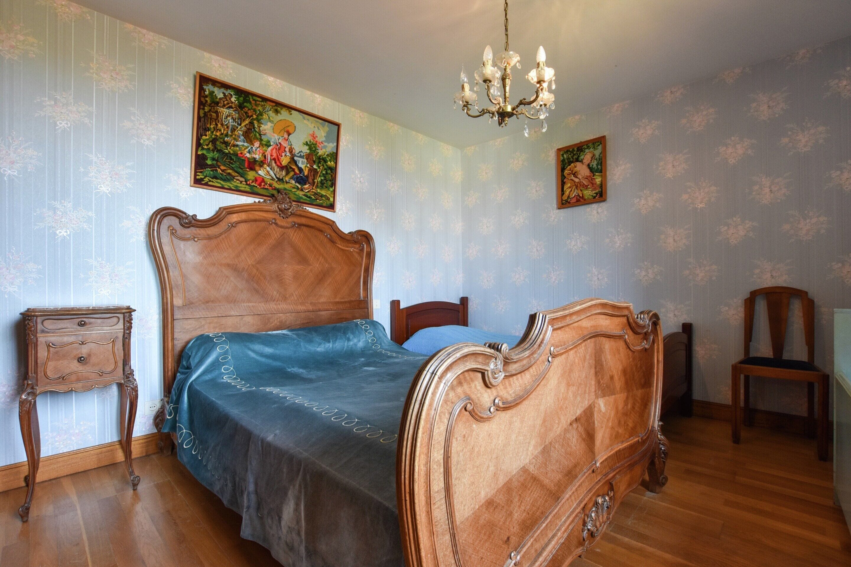 A bedroom with a wooden bed, a nightstand, a chair, and two wall-mounted paintings.