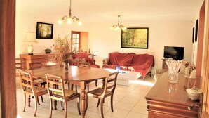 A dining area with a wooden table and chairs, a red sofa, and a TV in the background. - Historic Dordogne Escape (Loubejac)