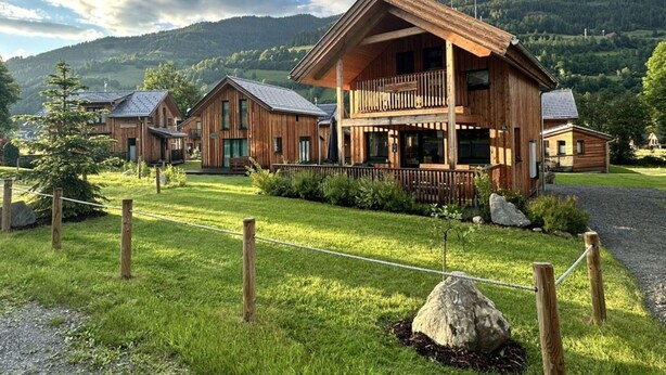 A wooden cabin complex with a large central building featuring a balcony, surrounded by smaller cabins, set in a grassy area with a mountainous backdrop. - Appealing Chalet Near ski Slope (Sankt Georgen am Kreischberg)