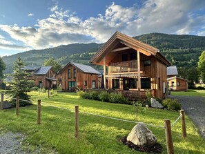 A wooden cabin complex with a large central building featuring a balcony, surrounded by smaller cabins, set in a grassy area with a mountainous backdrop. - Appealing Chalet Near ski Slope (Sankt Georgen am Kreischberg)