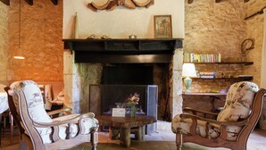 A rustic room with a fireplace, two upholstered chairs, a round wooden table, and a bookshelf. - Holiday Home in Dordogne Near Lascaux Cave (Les Eyzies)