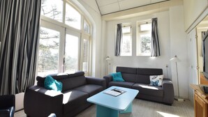 Una sala de estar moderna con dos sofás, una mesa de centro y ventanas grandes con cortinas.