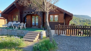 Eine Holzhütte mit Veranda, Sitzgelegenheit im Freien und Blick auf die Berge.